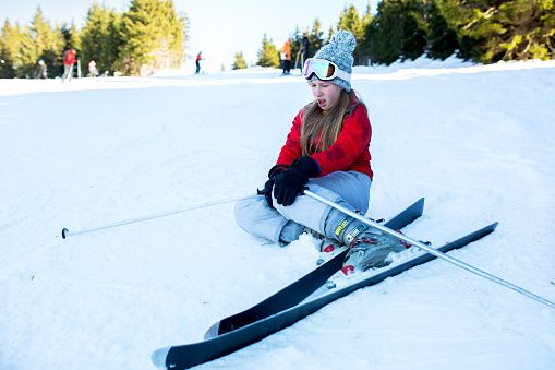 Teenage ski girl holding her knee in pain after accident on ski slope.